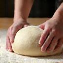 Manos de un panadero espolvoreando harina sobre una masa.